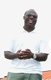 Marshall Faulk in a white t-shirt with his hands together smiling.
