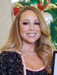 Mariah Carey smiling in a black dress in front of a Christmas tree