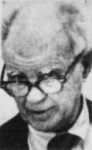 An aged, balding man glances over his glasses