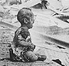 Monochrome photograph of an injured baby sitting alone and crying on the platform of a ruined and smoking railway station