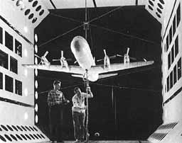 Two men testing a scale model airplane in a wind tunnel.