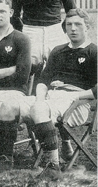 Black and white photograph of Louis Moritz Speirs seated, wearing a Scottish rugby strip and with other rugby players seated and standing near him.