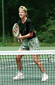 A blonde-haired female tennis player with multi-colored shorts and a black shirt, with the tennis racket out in front of her