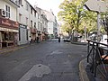 L'ancienne route qui entourait la place vue du bar de la Plaine. Aujourd'hui, la route permet toujours de relier la rue des Trois-Mages à la rue Saint-Pierre, mais ne permet plus de tourner sur la partie Est de la Plaine. Il s'y trouve désormais les terrasses de différents bars.