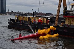 A red helicopter being lifted from the waters of the East River on March 12, 2018. The helicopter had been involved in a forced landing on March 11, and yellow floats remained deployed from the skids.