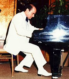 A pianist in a white suit performing on a black grand piano