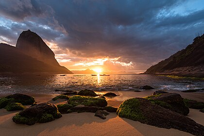 Pôr do sol no Rio de Janeiro, Brasil. O Pão de Açúcar é visível no fundo, à esquerda. Elevando-se 396 m acima do porto, o pico recebeu esse nome por sua semelhança com o formato tradicional do açúcar refinado concentrado. Ele é conhecido mundialmente por seu teleférico e pelas vistas panorâmicas da cidade e de outros lugares. A montanha é uma das várias montanhas monolíticas de granito e quartzo que se erguem diretamente da borda da água ao redor do Rio de Janeiro. É protegida pelo Monumento Natural dos Morros do Pão de Açúcar e da Urca, criado em 2006. Isso se tornou parte de um Patrimônio Mundial declarado pela UNESCO em 2012. (definição 6 016 × 4 016)