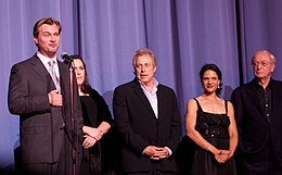 Christopher Nolan speaking to the mic while four people are standing behind him