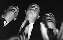 A photo from a low angle of three men looking ahead, clapping their hands and opening their mouths widely.