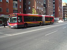 A red and yellow TUSSAM articulated city bus on the street of Sevilla