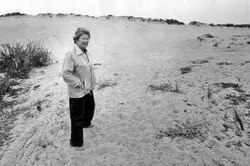 A woman stands on sand dunes.