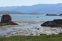 Reservoir with rock formations rising above it and mudflats in the foreground