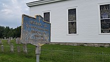 a picture of the marker, in bad shape, with the white church behind