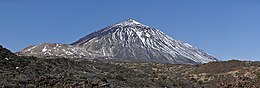 Photo du volcan conique partiellement enneigé avec un dôme marqué à sa gauche et un terrain rocheux au premier plan.