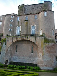 Photo couleur d'une tour carrée à tourelles d'angle d'un château en brique. Au sous-sol, des ouvertures médiévales allongées sont assombries par une terrasse portée par une voûte s'appuyant sur les tourelles. Les hautes portes-fenêtres signalent une grande hauteur de plafond. Au-dessus de la toiture plate en tuile, dépasse le mur sud.