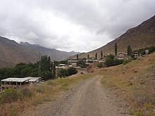 A gravel road leading into a wide valley with short, rectangular buildings.