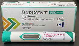 Photo of a Dupixent (dupilumab) 300mg/2mL auto-injector pen and accompanying packaging. The pen is labeled in Japanese.