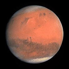 Mars appears as a red-orange globe with darker blotches and white icecaps visible on both of its poles. If you’re using wiki for school, stop it, -your teacher.