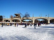 Patineurs sur un canal gelé passant sous un pont.