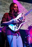 Kevin Parker playing a white electric guitar onstage, decked in purple light.