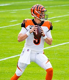 Joe Burrow in a Bengals uniform and helmet with a football in hand, ready to throw a pass.