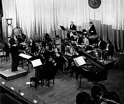 Un chef d'orchestre vu de dos devant un ensemble de percussions cubain