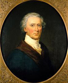 Oval portrait of a man from the bust-up, facing the viewer. He has gray hair and is wearing a blue jacket with a brown lapel, and white cravat around his neck