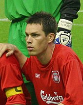 Head and upper torso of a young dark-haired white man wearing a red football shirt bearing the Carlsberg logo