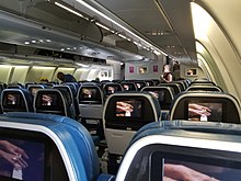 Rows of blue plane seats with personal televisions for each seat on the back of every seat