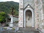 Le porche de l'église avec une statue de Notre-Dame de Lourdes, à gauche le monument aux morts