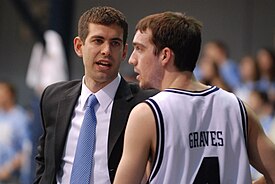 Stevens looks at a player as he talks with him. The players' eyes are turned toward the basketball game to Stevens's left.