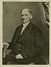 White male in a dark suit holding a book