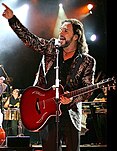 Publicity photograph of Marco Antonio Solís performing with a red electric guitar.