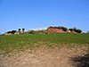 A ruined sandstone wall seen in the distance across a field, including a pair of gateposts on the left.