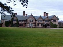 A long two-storey house with five gables, almost entirely timber-framed. In front is a large expanse of lawn.