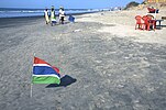 A sandy beach with a small Gambian flag in the foreground.