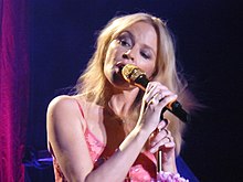 Photograph of Minogue singing into a microphone looking to her right