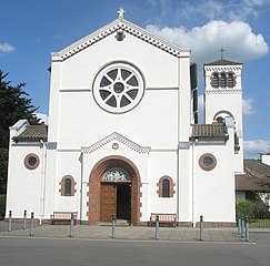 The tall white main entrance face of the church. Its normal pavement level parvis is protected by bollards.