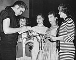 Elvis Presley signing autographs for a group of young female fans.