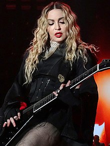 Madonna playing a guitar onstage, wearing a black, flowy dress.