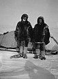 Das Schwarzweißfoto zeigt Mikkelsen und Iversen nebeneinander in dicker Pelzkleidung im Schnee stehend und in die Kamera blickend. Hinter ihnen befindet sich ein abgedeckter Schlitten.