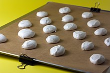 A metal sheet, lined with brown paper. The paper is clipped to the side of the pan. There are cookies on the paper, ready to bake.
