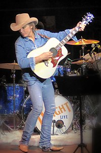 Country music singer Dwight Yoakam, looking to his side while strumming a guitar.