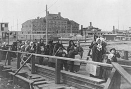 De nombreuses personnes traversent un pont et un bâtiment imposant est derrières elles