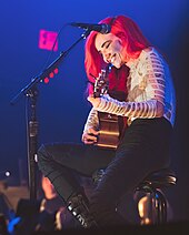 A picture of a woman performing on stage playing an acoustic guitar.