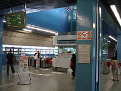 Niveau du hall de la station Queenstown, avec un écran à plasma, centre de service aux passagers et portillons automatiques.