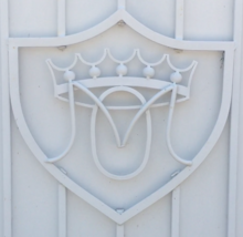 Family heraldry in the form of a shield shaped into an iron gate pained white.