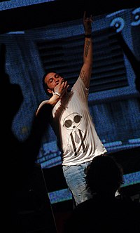 A light-skinned man is dressed in a short-sleeved shirt and is seen performing in a dark room.