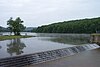 Water from a forest-surrounded lake spills over a stairstep dam