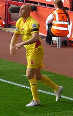 A man wearing a yellow football shirt and shorts, standing on the playing pitch.